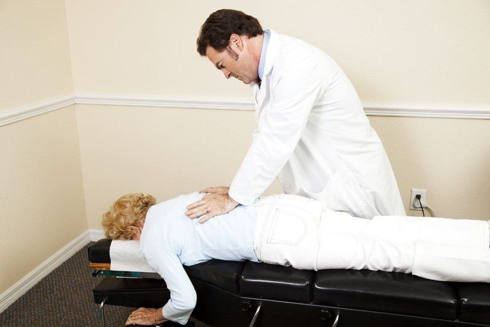 A chiropractor treats an elderly woman's back injuries.