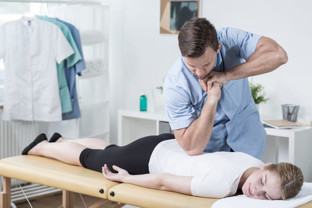A chiropractor is administering chiropractic treatment on a young woman's middle back.