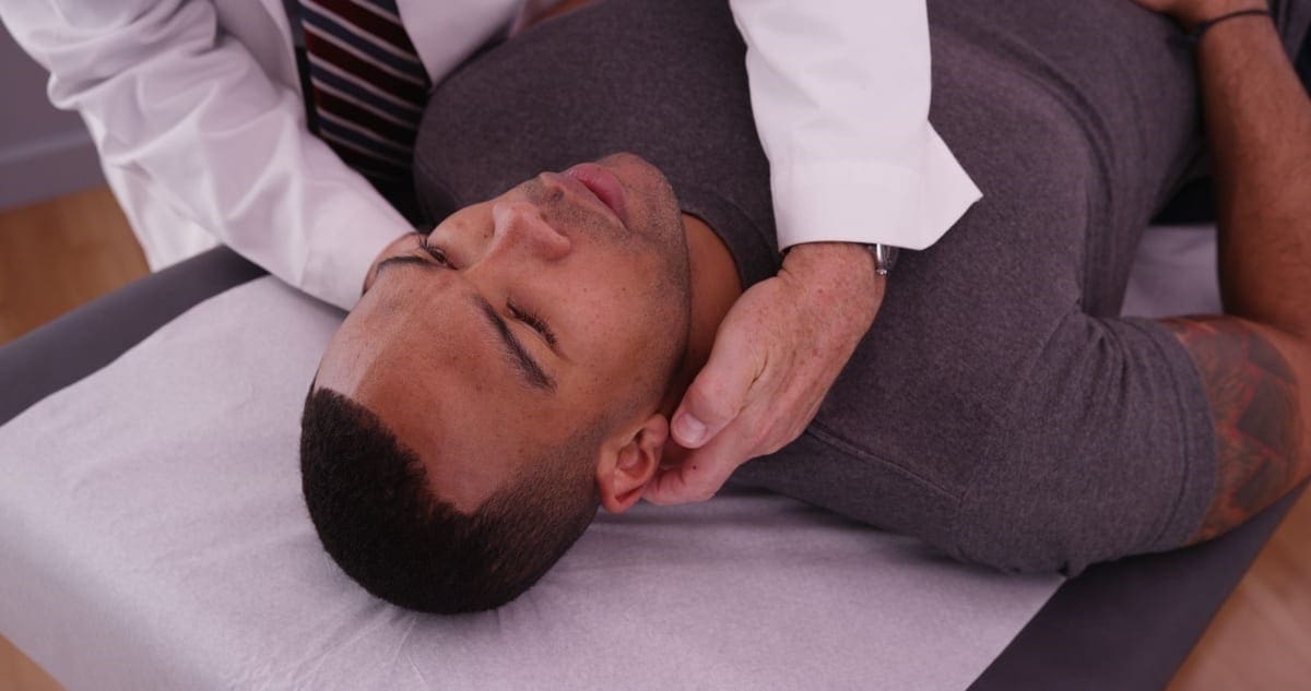 A chiropractor is administering a neck adjustment on a male patient.