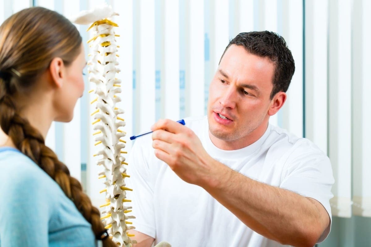 A chiropractor explains the causes of back pain from injury to a patient using a model spine.
