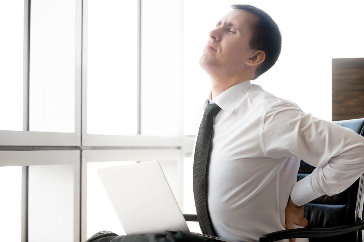 A man stretches at his work desk because of lower back pain.
