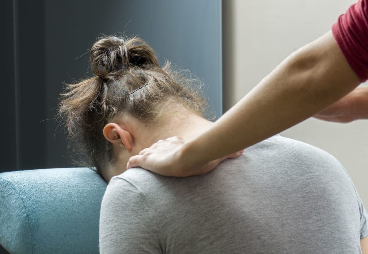 A woman is being treated by a chiropractor for hypertension in the upper back and shoulders.