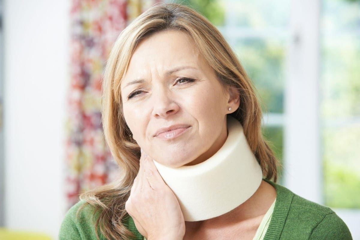 A woman in a neck brace winces in pain.