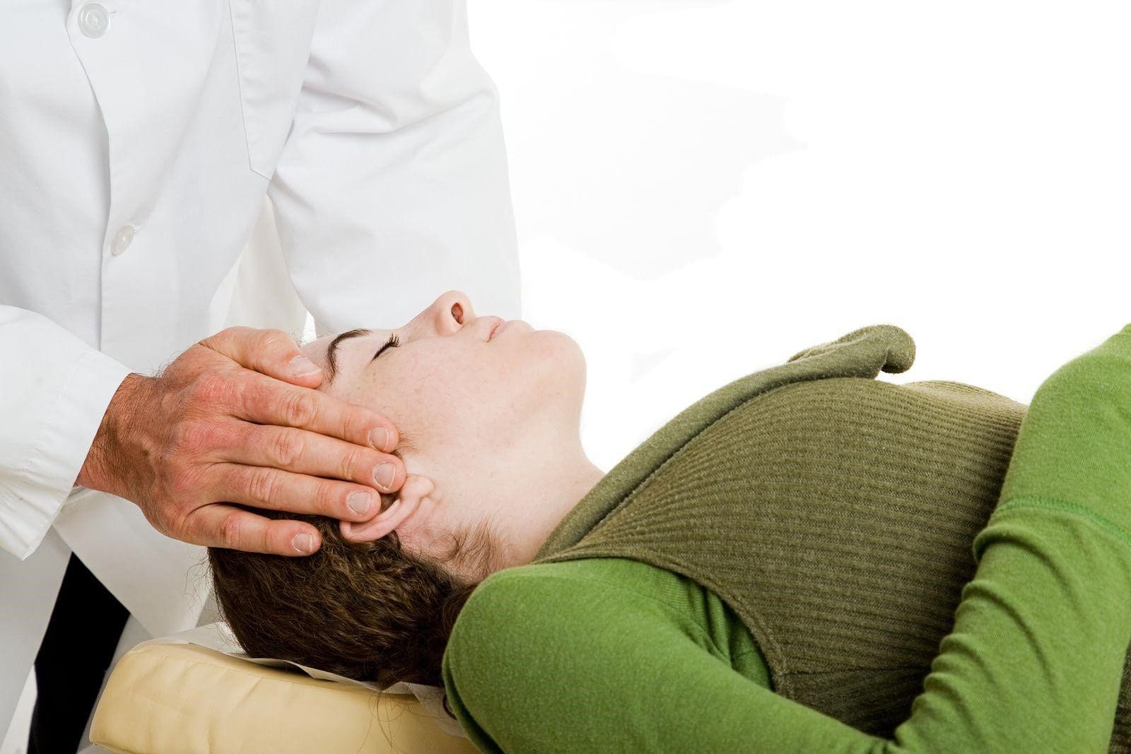 A woman is laying on a chirpractic table and being treated for migraines by a chiropractor.