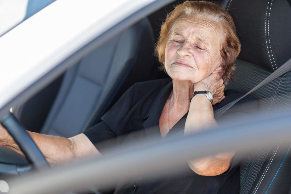 An older woman holds the back of her neck in pain after a car accident.