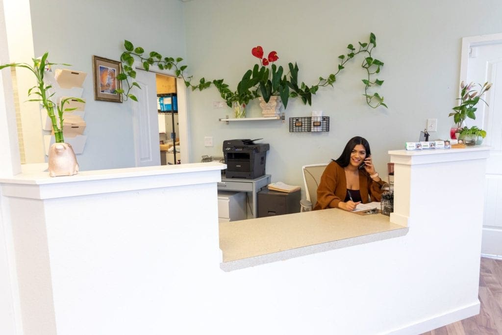 The receptionist at Tigard Chiropractic is smiling while talking to a patient on the phone.