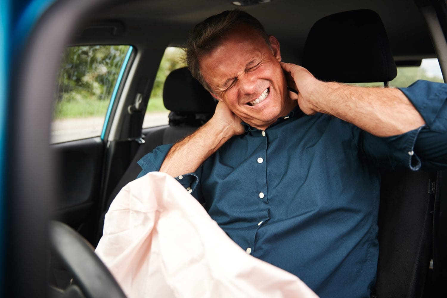A man is grimacing from neck pain after a car accident.