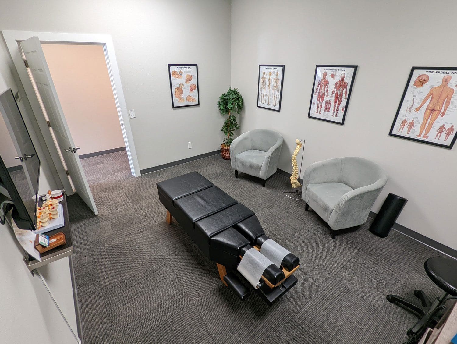 Woodburn chiropractic treatment room with adjustment table and sitting chairs.