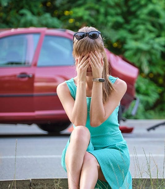 A woman sits on the curb after a car accident looking distraught.