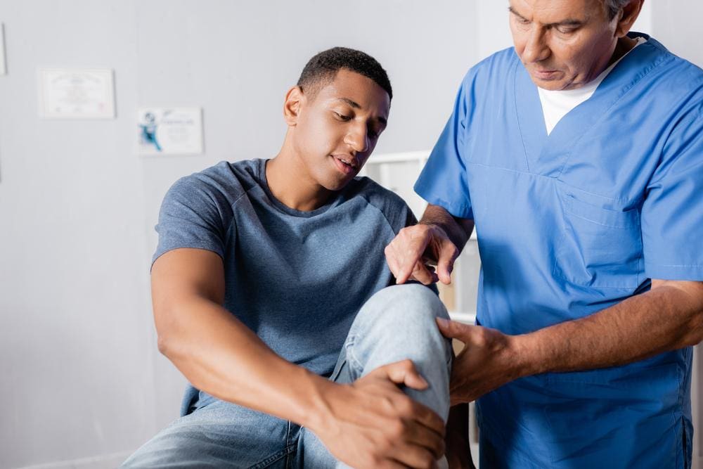 A chiropractor examines a man's knee, to create a treatment plan for knee pain.