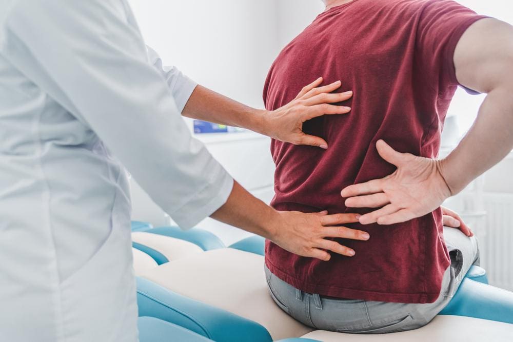 A chiropractor is examining a man's back to prepare for treatment of middle back pain.