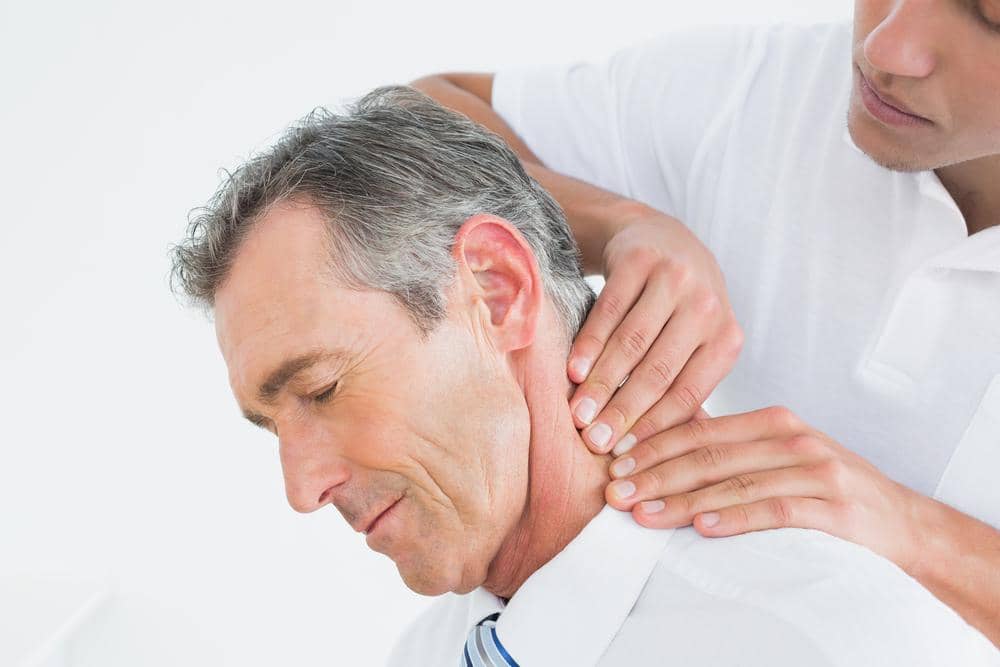 A chiropractor is adjusting a man's neck to treat lower neck pain.