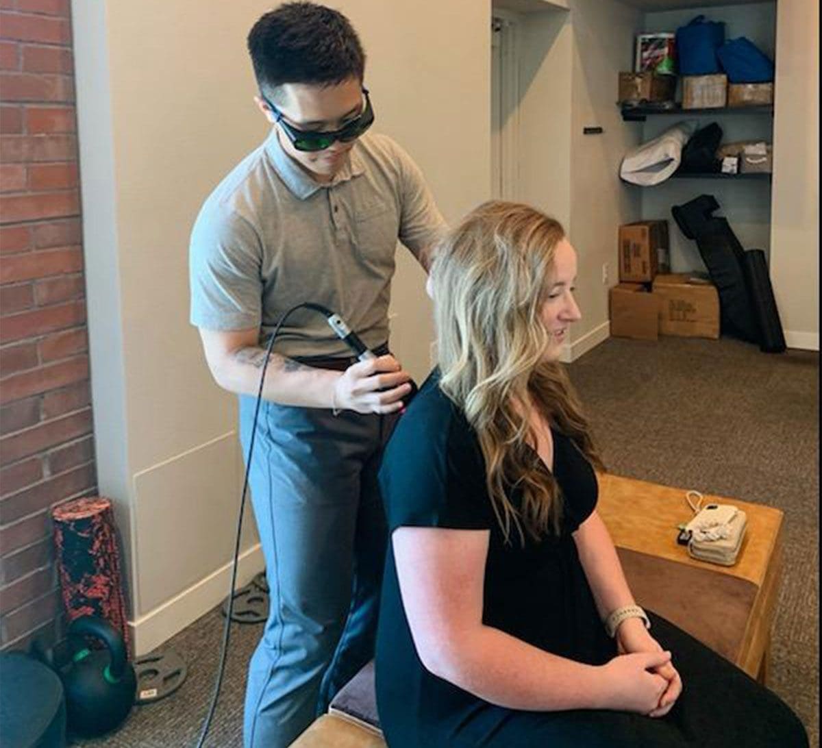 A Chiropractor administering laser therapy on a female patients back.