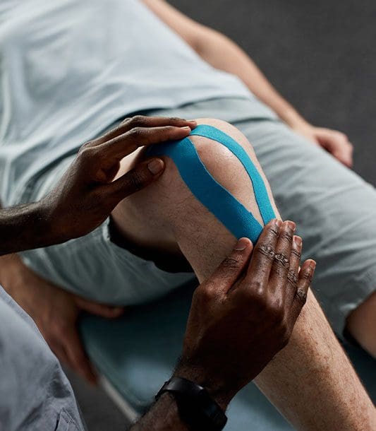 A chiropractor is treating a man for muscle injury strain in the knee.