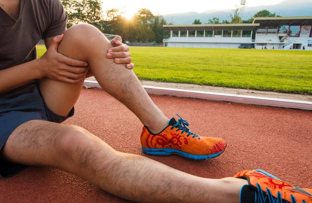 A man sits on a running track because his knee hurts from a knee injury.