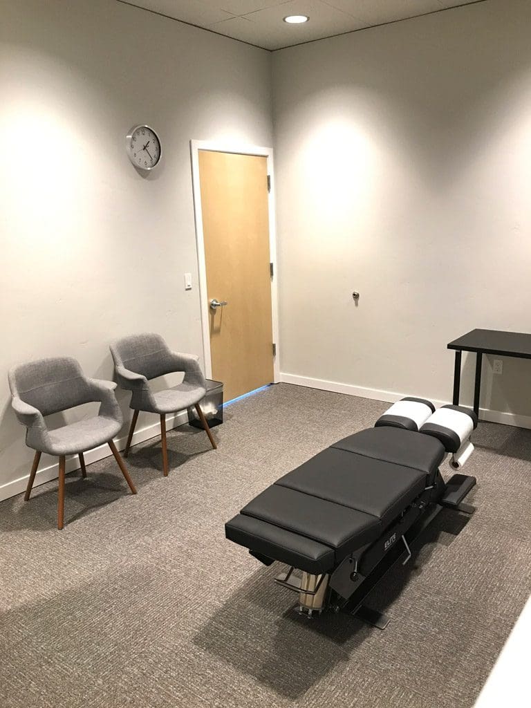 Bend Clinic adjustment room with chiropractic table and two chairs