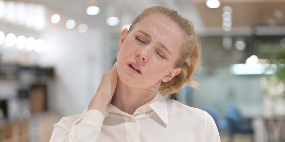 A woman suffering from neck pain leans her head to the left stretch her neck.