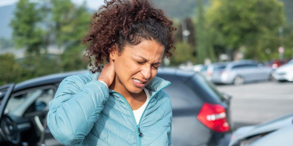 A woman is holding the back of her neck and wincing in pain after a car accident.