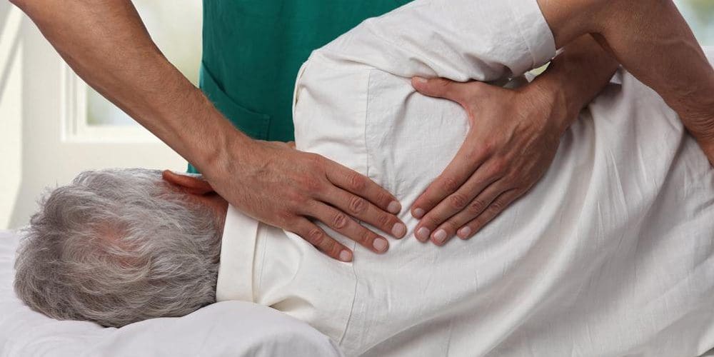 A chiropractor is treating an elderly man for shoulder pain.