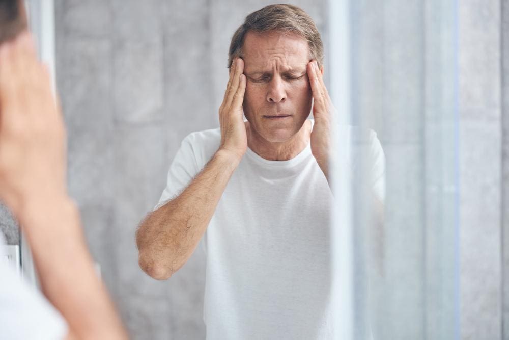 A man rubs his temples because he struggles with dizziness from migraines. 