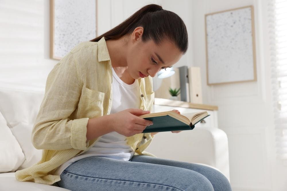 A woman has bad posture while hunched over reading a book.