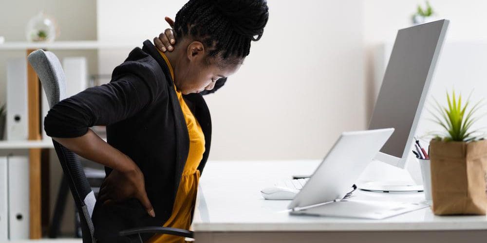 A woman sitting at a work desk is experiencing back pain from bad posture.