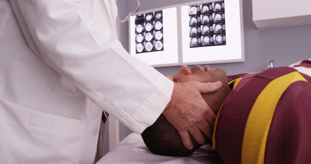 A chiropractor is treating a man to alleviate symptoms of a concussion. 