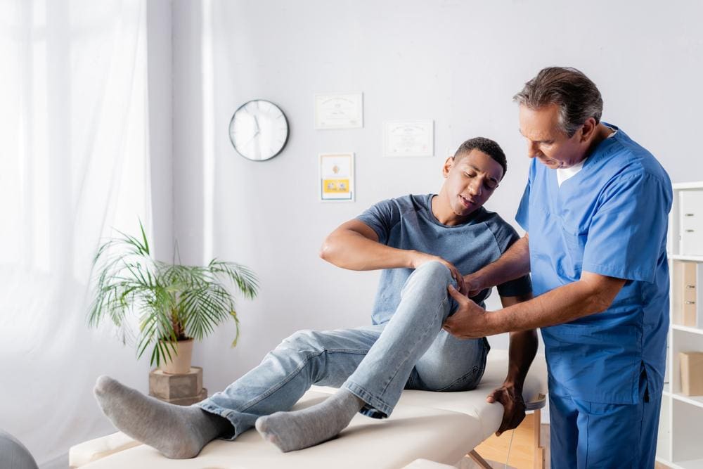 A chiropractor is examining a man's knee for a bursitis injury.