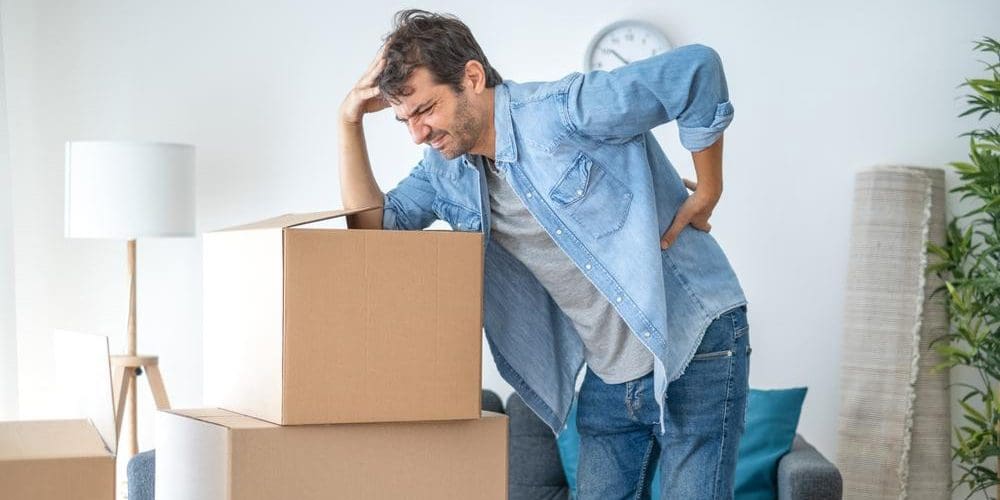 A man cannot stand up straight after pulling a muscle in his back after lifting heavy boxes.