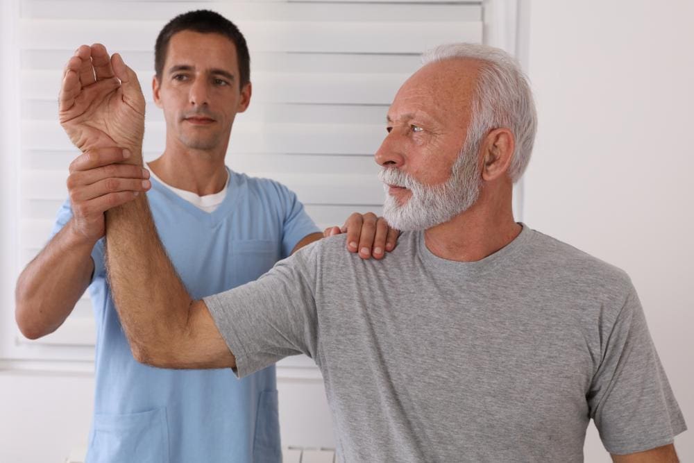 A chiropractor is treating an elderly man for joint pain in his shoulder. 