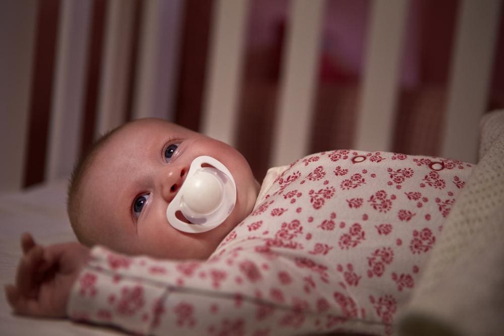 A baby with a pacifier laying in a crib.

