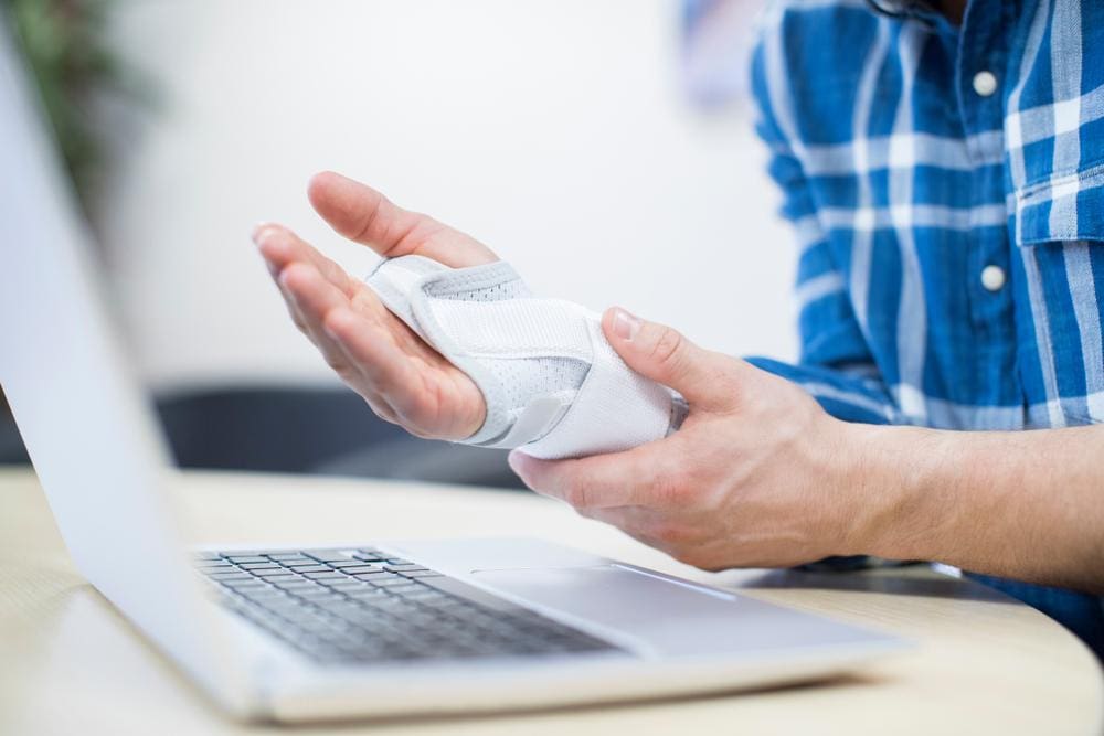 A man is having trouble typing because his wrist is in a cast because of carpal tunnel.
