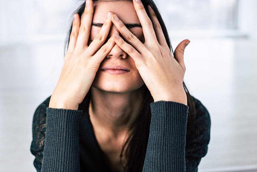 A woman is covering her face with her hands because is is very stressed. 