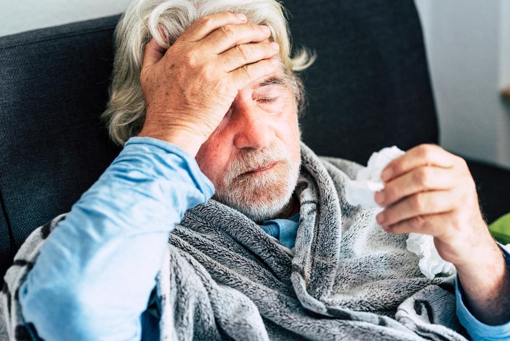 A man holding tissues and looking miserable because he is suffering from Covid. 