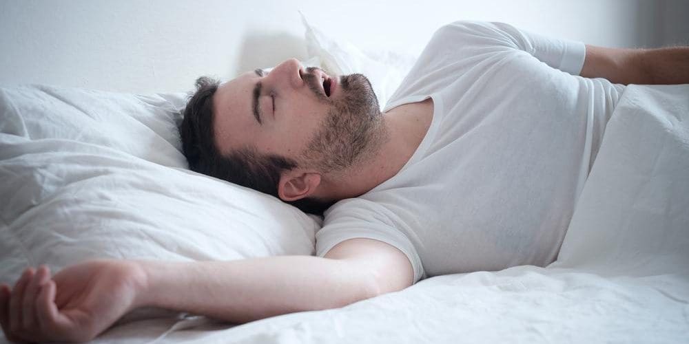 A man is sleeping but his breathing very shallow because he suffers from sleep apnea.