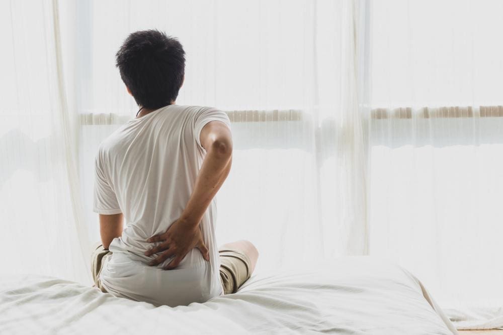 A person is struggling to get out of bed because of back pain.
