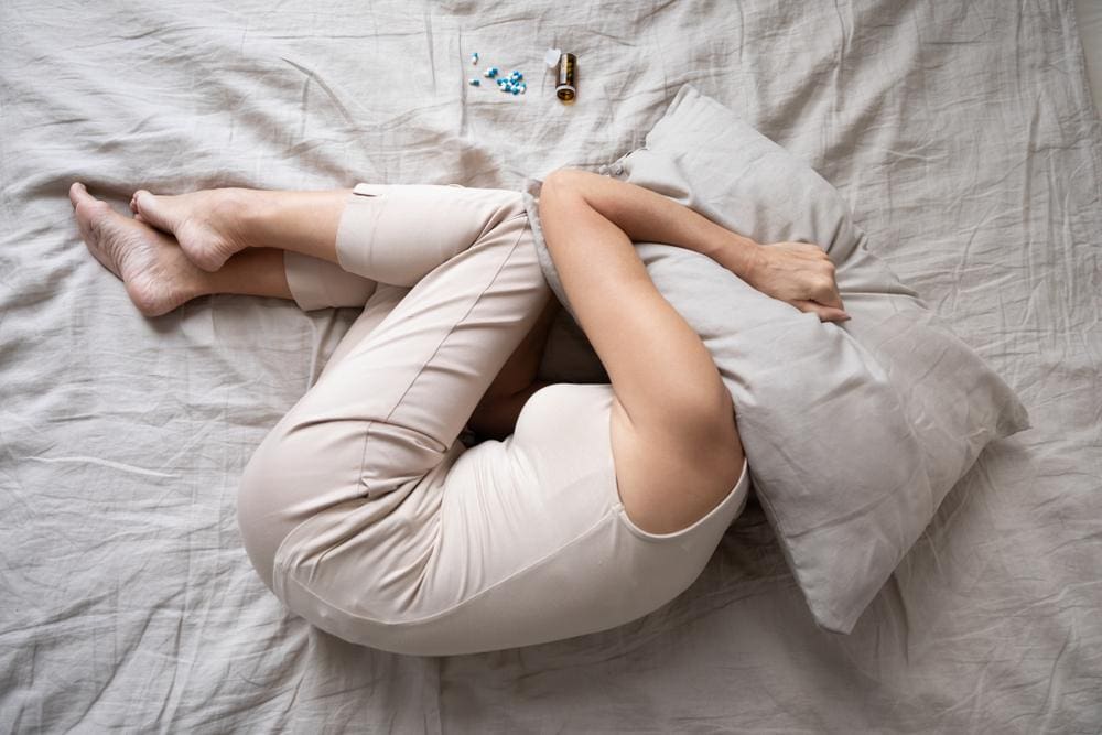 A woman
 is lying in the fetal position in bed with a pillow over her head because she suffers from chronic pain.