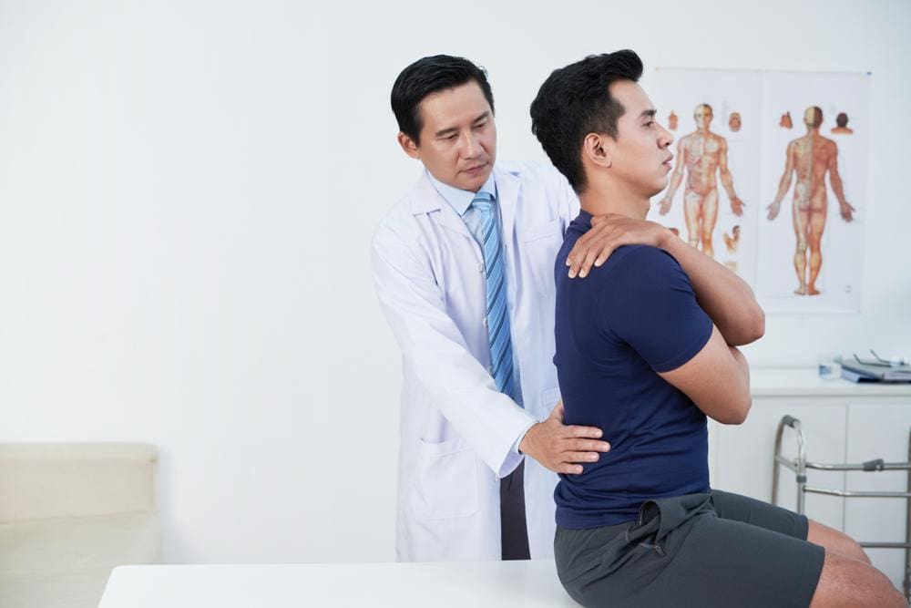 A young man is being examined by a chiropractor to determine treatment for a herniated disc caused by a car accident. 