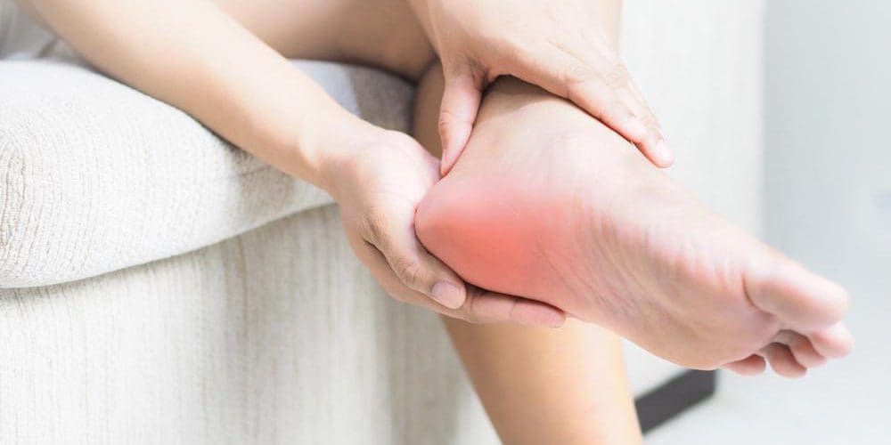 A person is rubbing their foot because of heel pain.