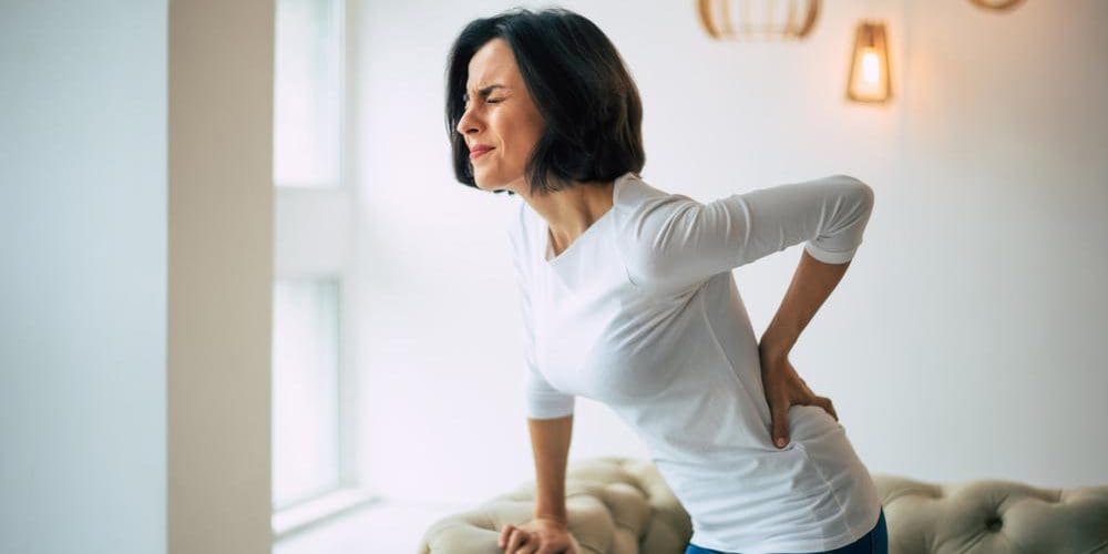 A woman is wincing in pain and having trouble standing up straight because of herniated disc pain.