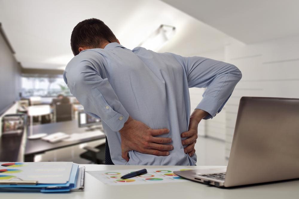 A man is in pain while sitting at his work desk, because of a herniated disc.