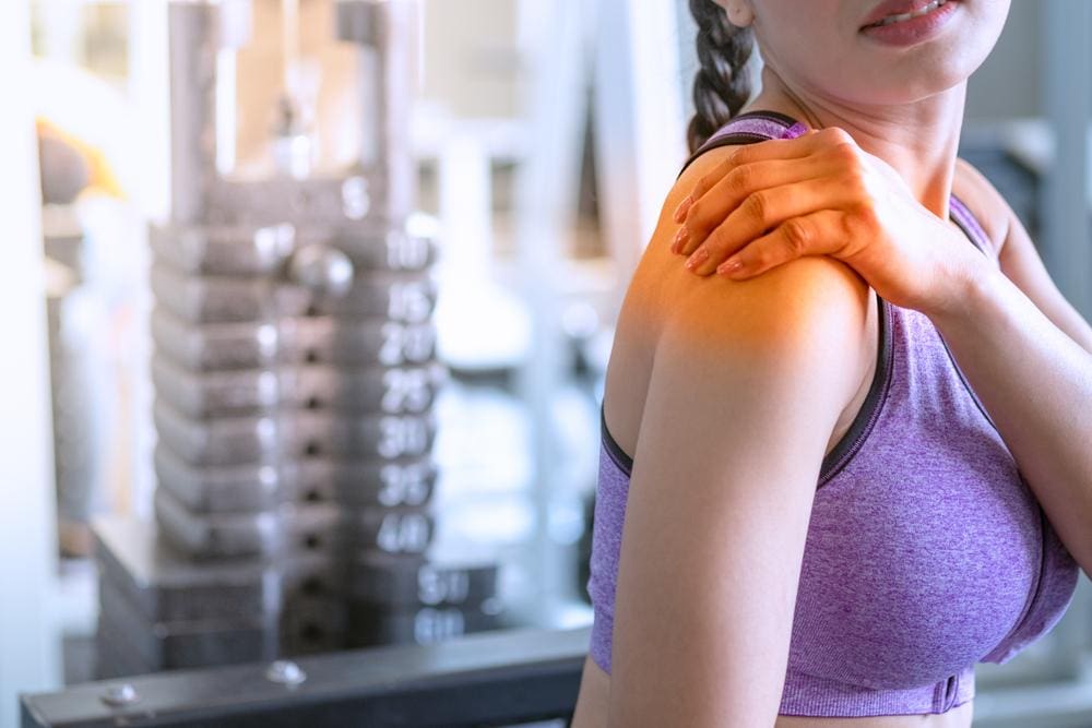 A woman is holding her shoulder because of pain from a rotator cuff injury. 