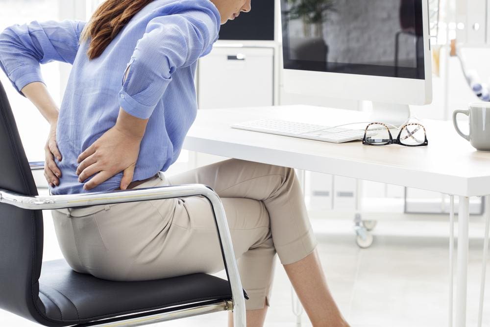 A woman is experiencing back pain while sitting at her work desk, because of a slipped disc.