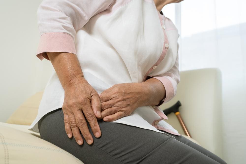 An elderly woman is having trouble standing up because of hip flexor pain.
