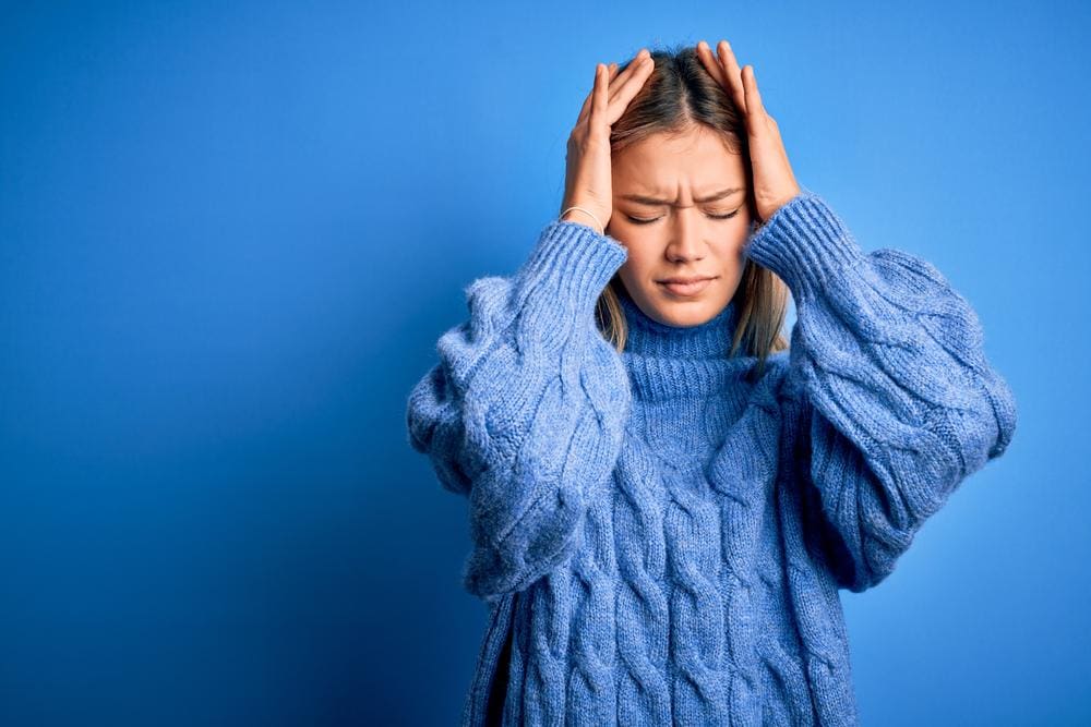 A woman in a blue sweater is suffering from headache pain.
