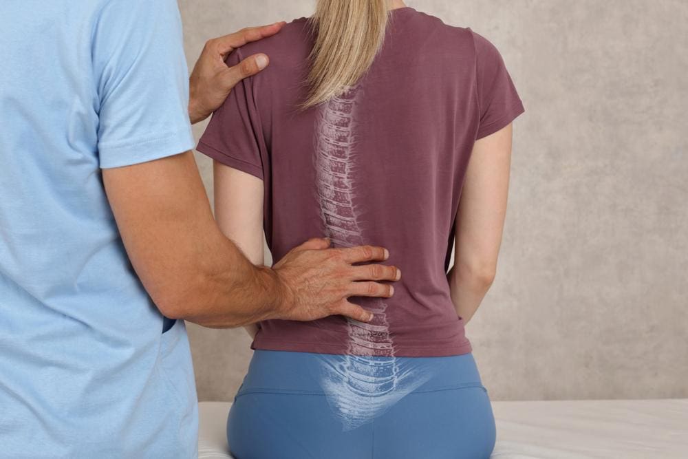 A chiropractor is examining a woman's back who had spinal fusion surgery. 