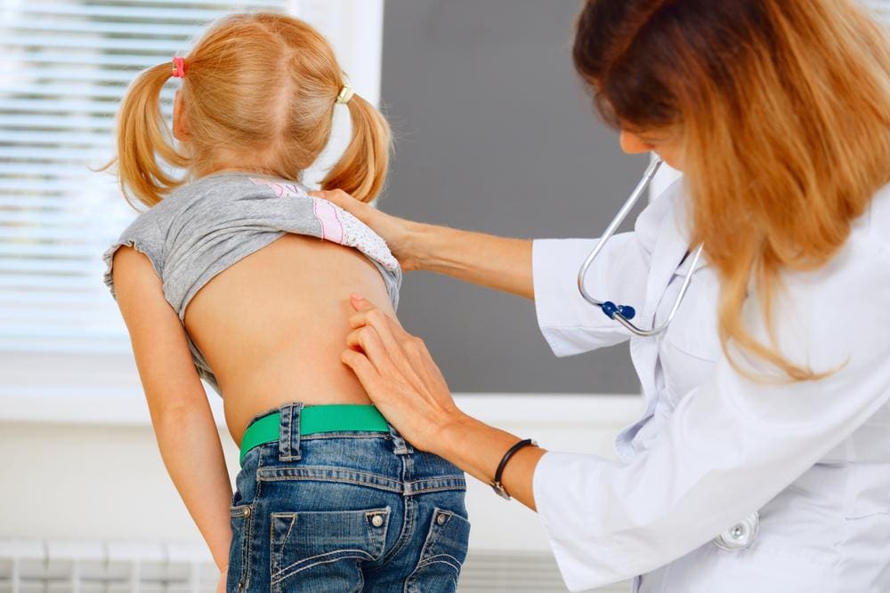 A child is getting checked for scoliosis. 
