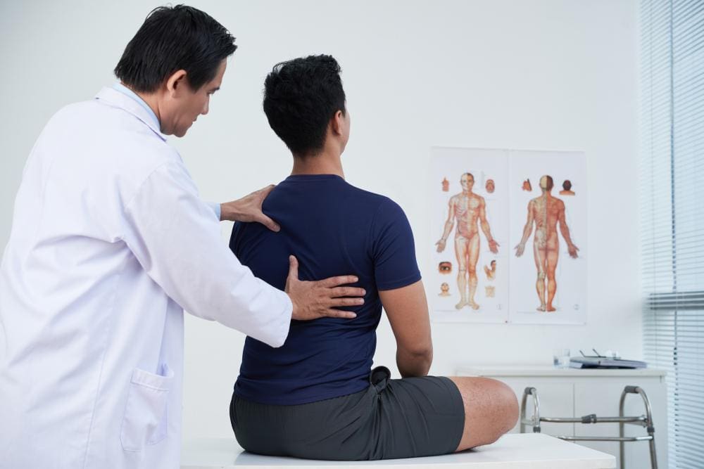 A chiropractor is administering an adjustment to a male patient to help manage pain. 
