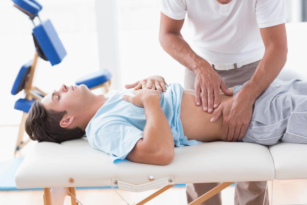 A chiropractor is treating a man for stomach problems. 