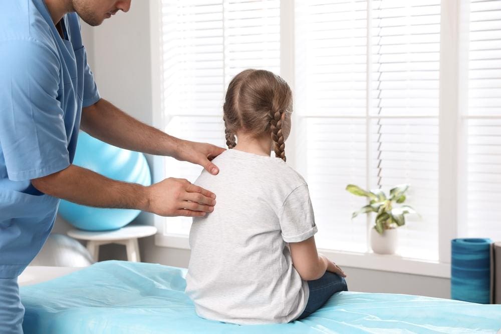 A chiropractor is examining a young girls spine to assess the right childhood treatment.